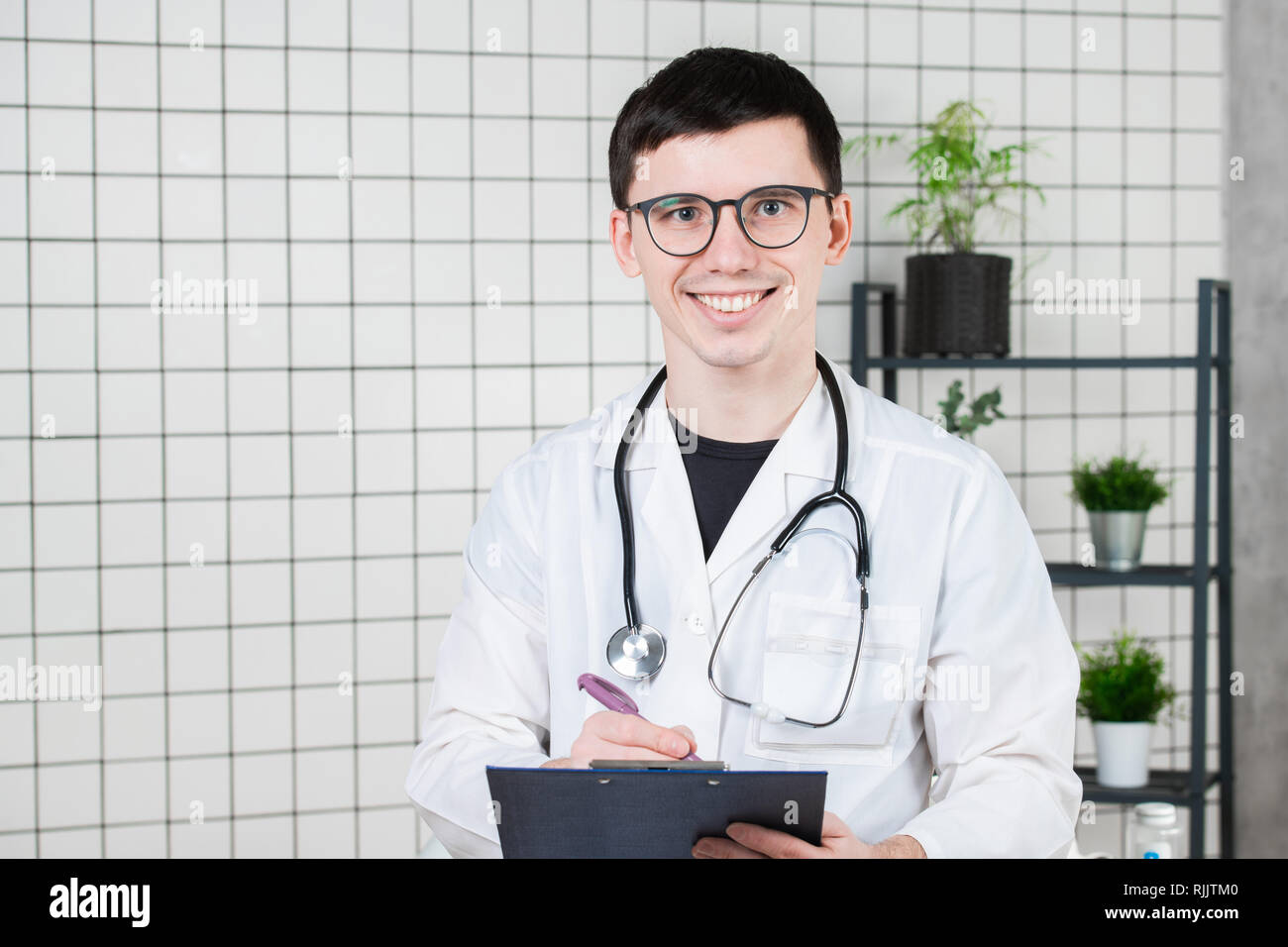 Happy smiling young doctor writing on clipboard in a modern hospital Stock Photo