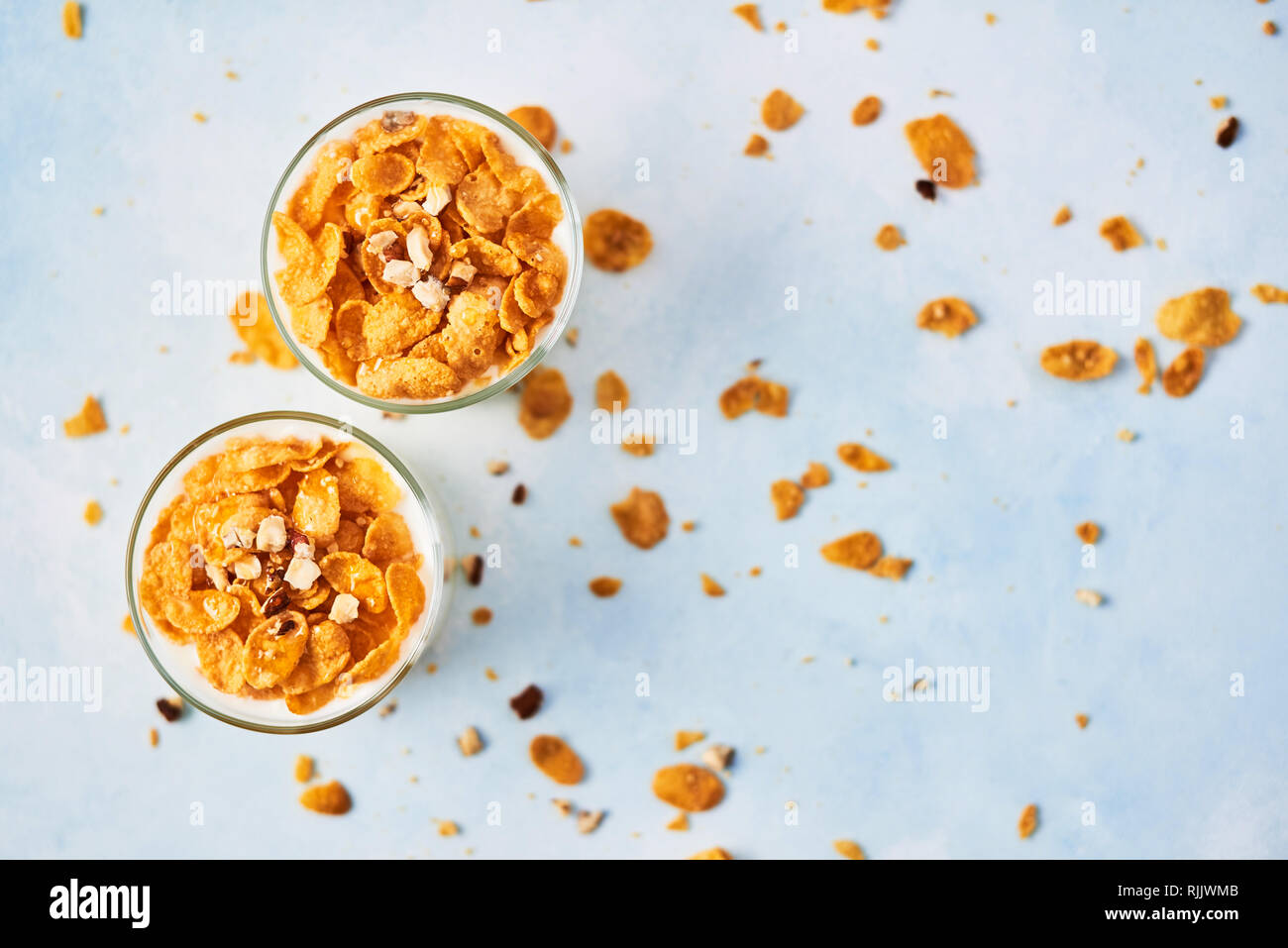 Healthy breakfast or dessert. Tasty corn flakes with yogurt, almond and honey in a small glass on light blue background. Top view. Copy space for text Stock Photo