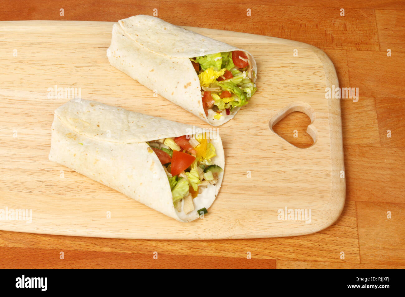 Chicken and sald sandwich wraps on a wooden chopping board with a heart shaped cutout Stock Photo