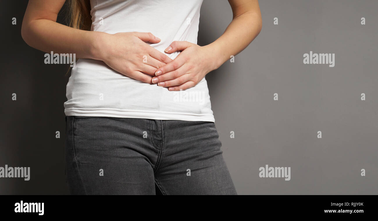 unrecognizable young woman holding her stomach with both hands - concept for dysmenorrhea, abdominal pain, bellyache, stomachache, painful periods or Stock Photo