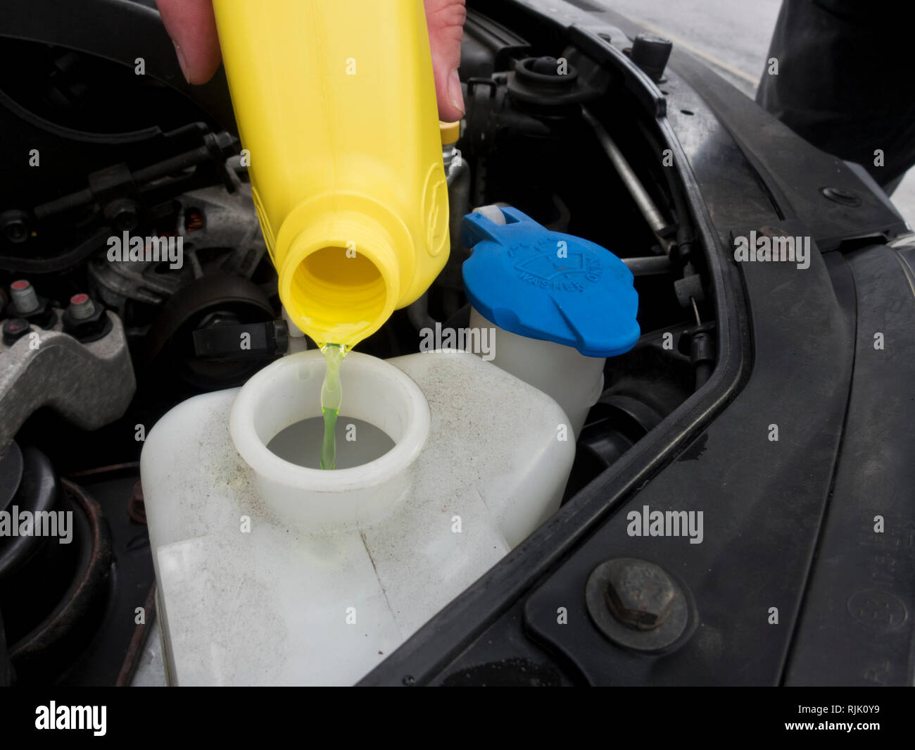 Caucasian Man Pouring Coolant or Anti Freeze Into an Antifreeze Reservoir Bottle, Part of a Car Engine Maintenance Routine Stock Photo