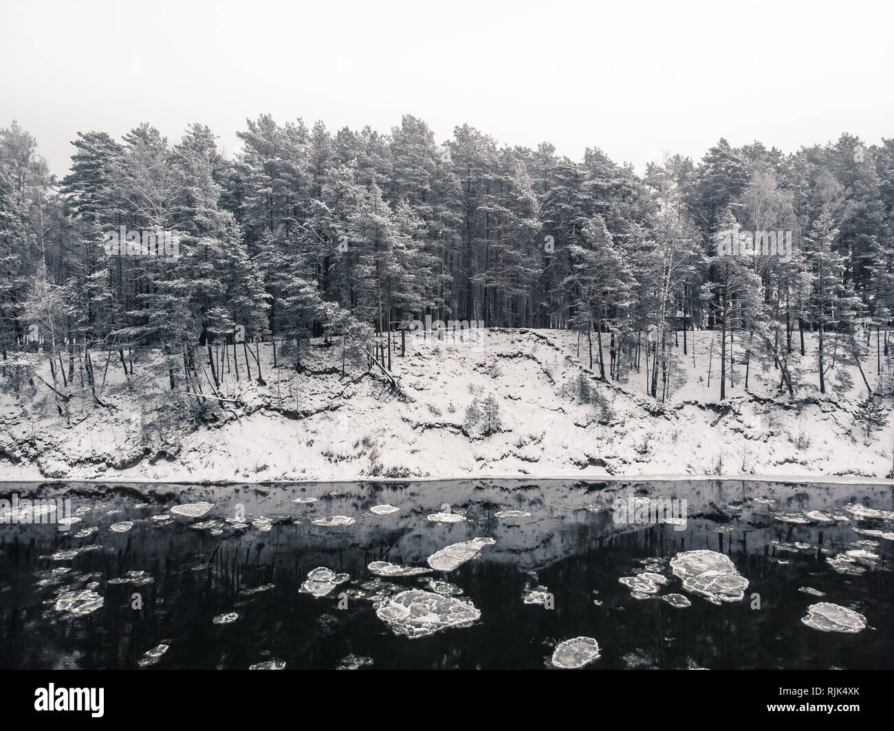 View to the snowy shore from the middle of freezing river with reflections of the forest in water Stock Photo