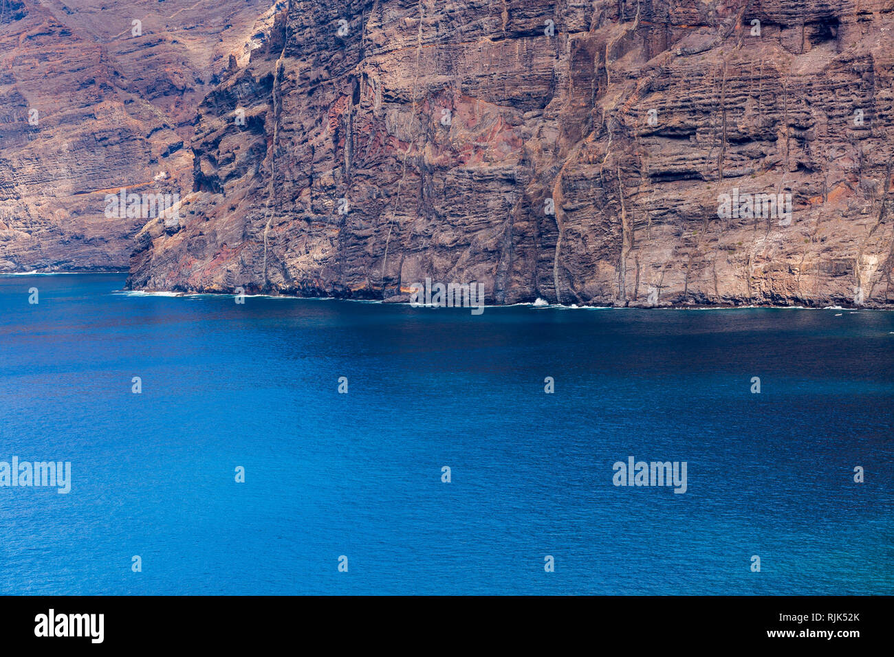 Sheer seacliffs of Los Gigantes  with seamed rugged rock faces meet the calm blue atlantic ocean on the west coast of Tenerife, Canary Islands, Spain Stock Photo