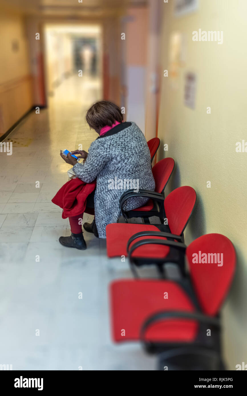 woman with smarthphone sitting in doctor's waiting room alone in large croridor Stock Photo