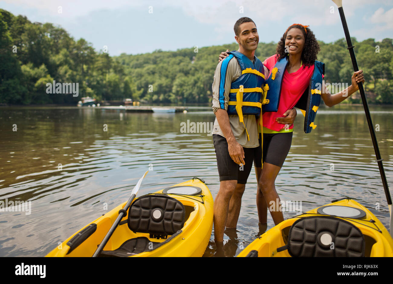 Portrait of a smiling young couple embracing in front of their kayaks. Stock Photo