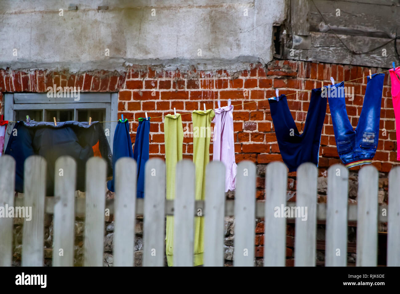 Clothes and clean washed laundry are dried behind the fence. Inner yard with clothes and linen drying on the ropes in Latvia. Colorful clothes laundry Stock Photo