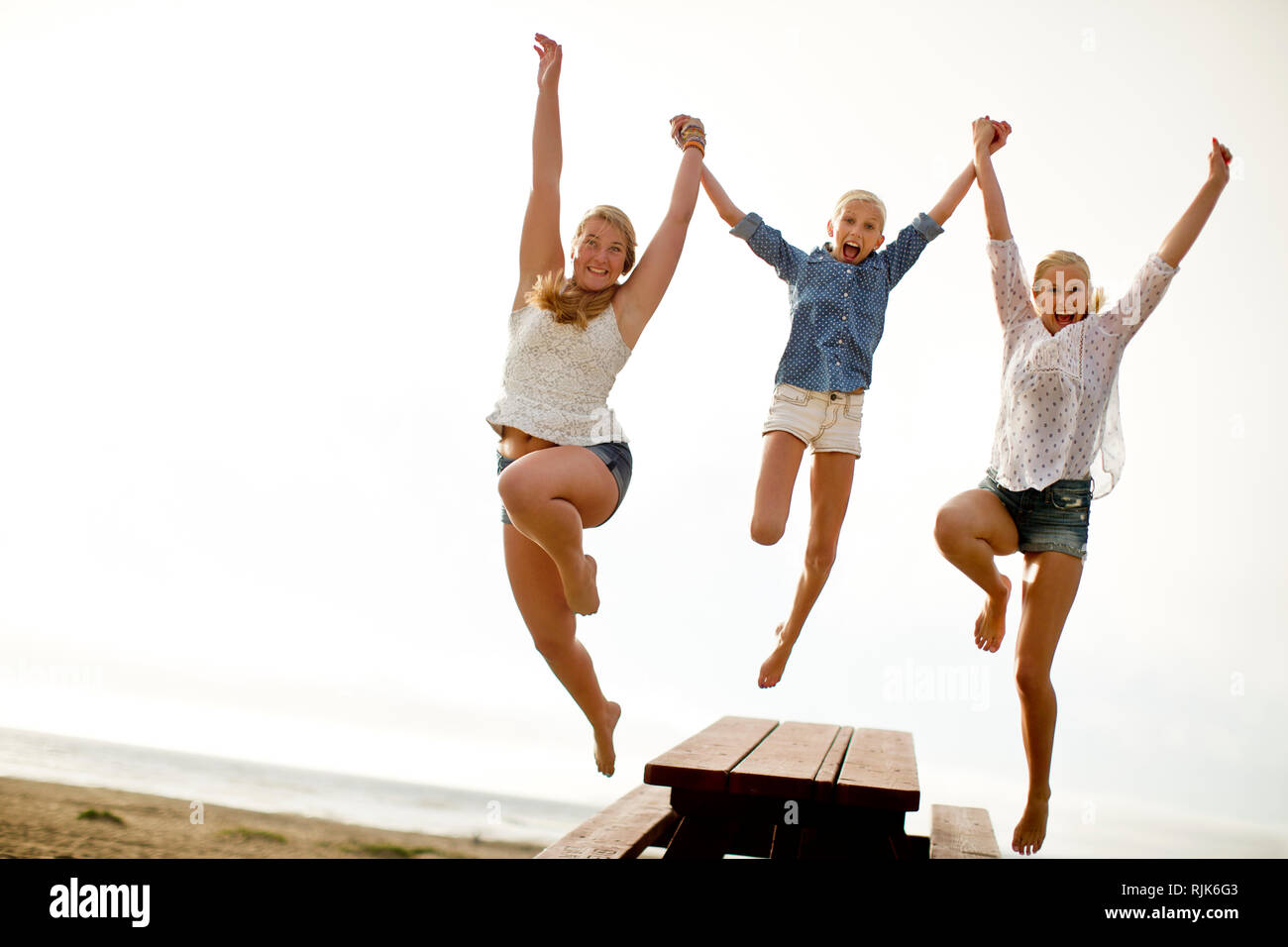 Portrait of three smiling sisters jumping on a beach. Stock Photo