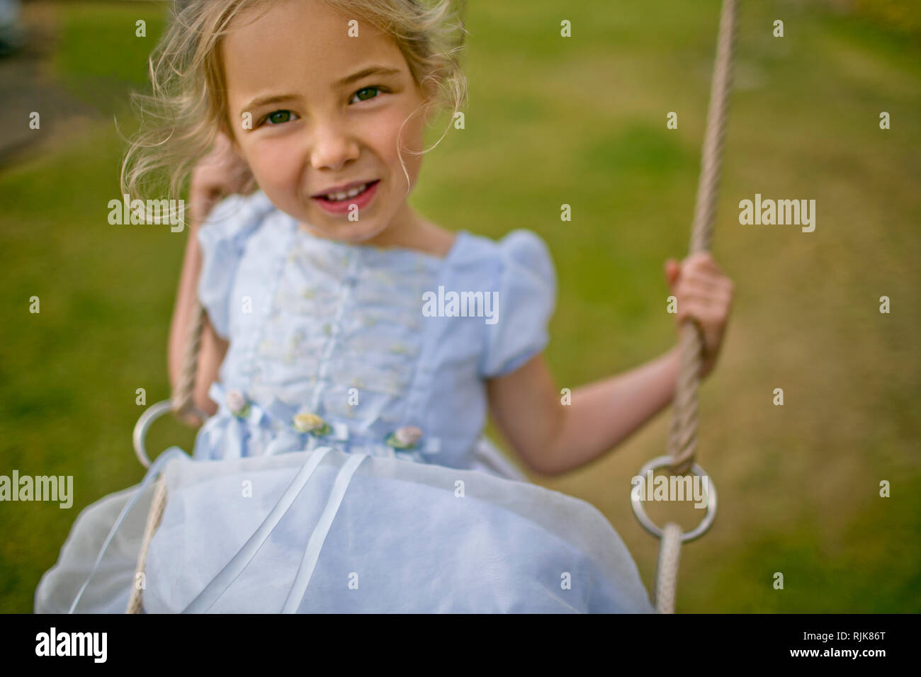 Portrait of a little girl playing on a swing in the back garden. Stock Photo