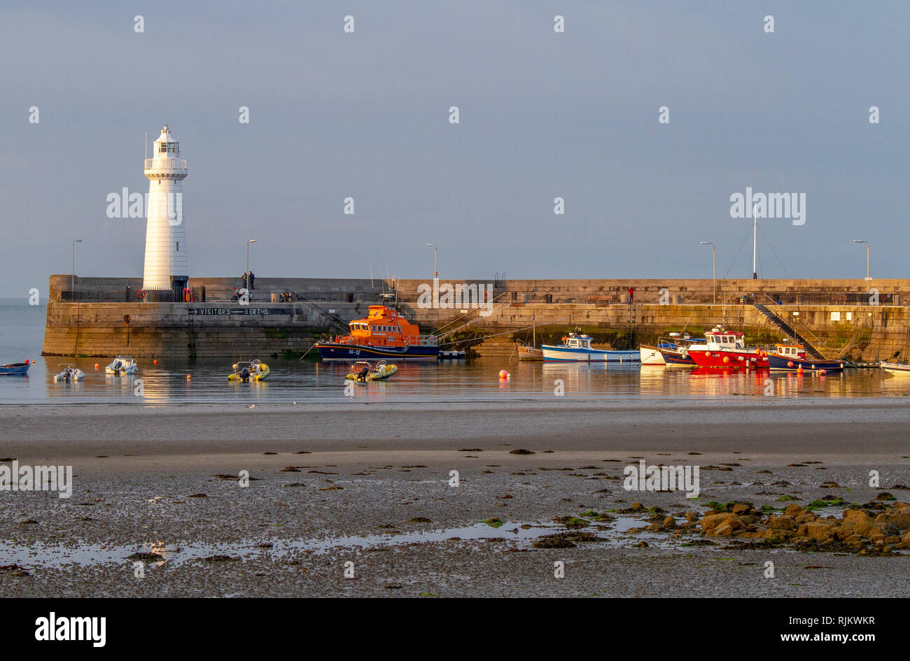 Harbour lighthouse and boats in harbour at low tide on sunny evening. Donaghadee Harbour, County Down, Northern Ireland. Stock Photo