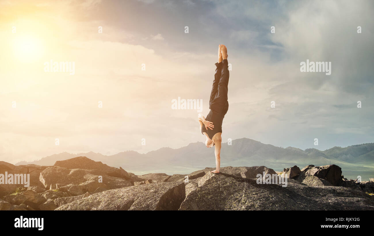Amazing yoga man doing one handstand on rock edge. Mixed media Stock Photo