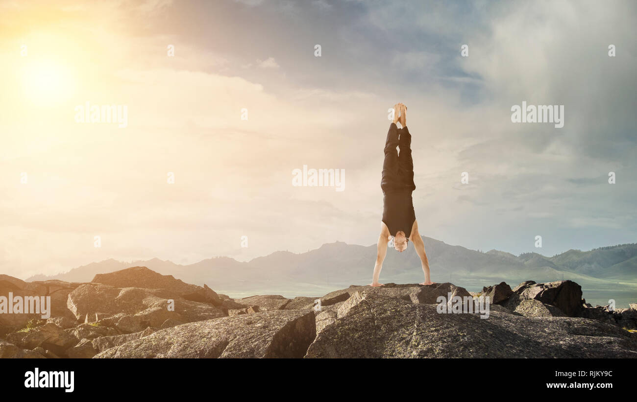 Amazing yoga man doing one handstand on rock edge. Mixed media Stock Photo