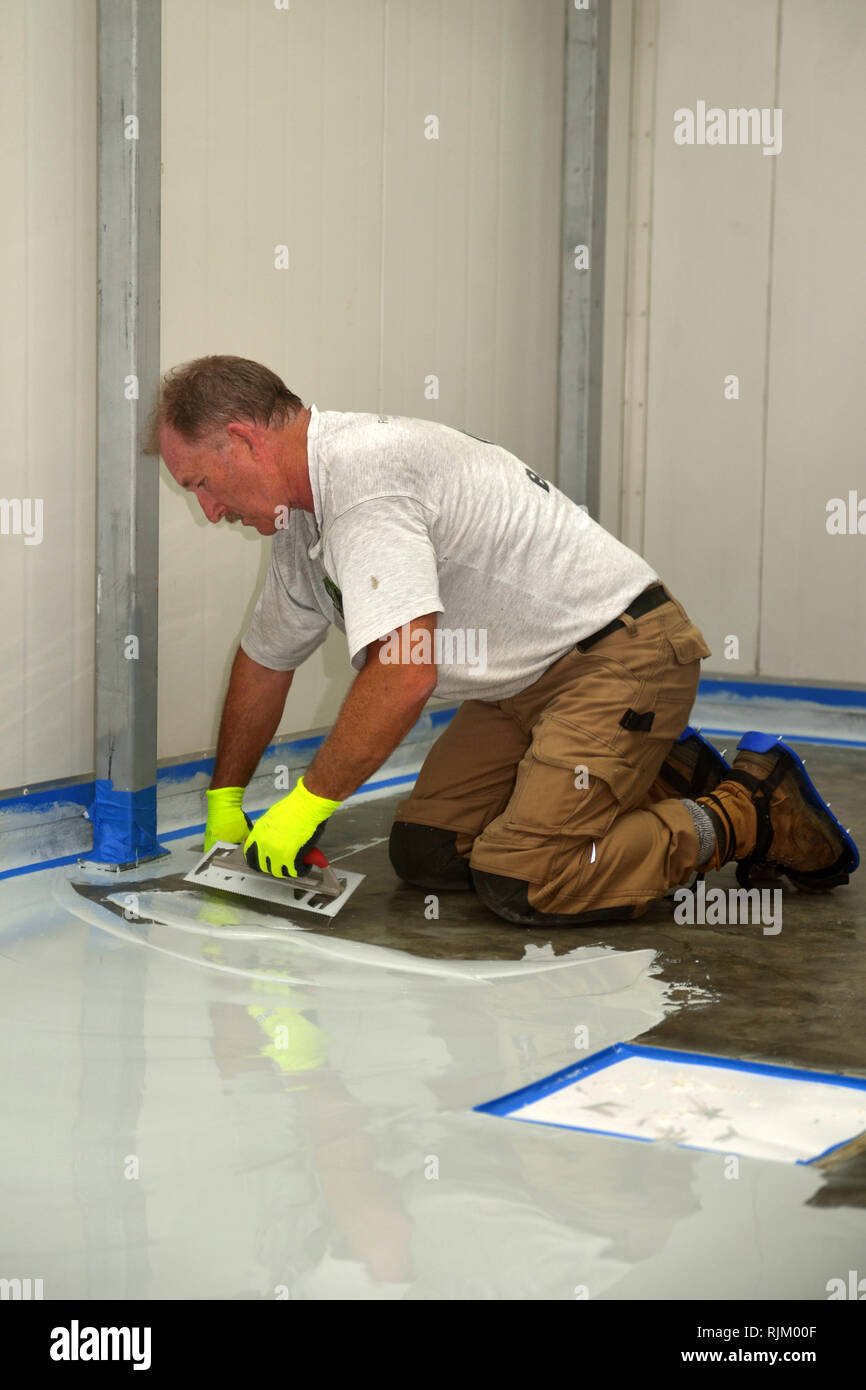 tradesman applying epoxy product to floor of an industrial building Stock Photo