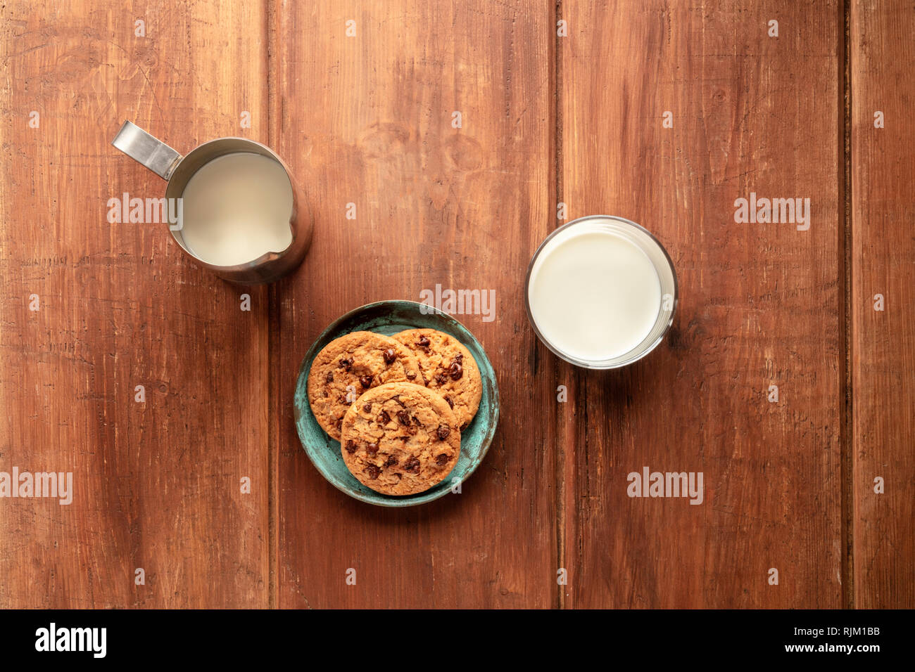 Chocolate chip cookies on a dark rustic wooden background, shot from the top with a milk jug and glass and copy space Stock Photo
