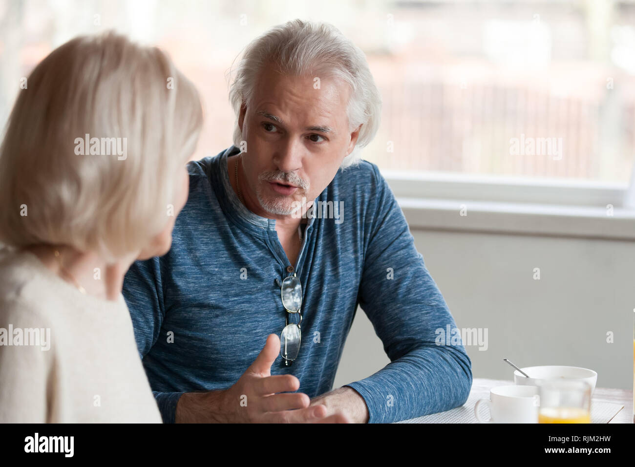 Senior spouses talking sitting together at table focus on husband Stock Photo