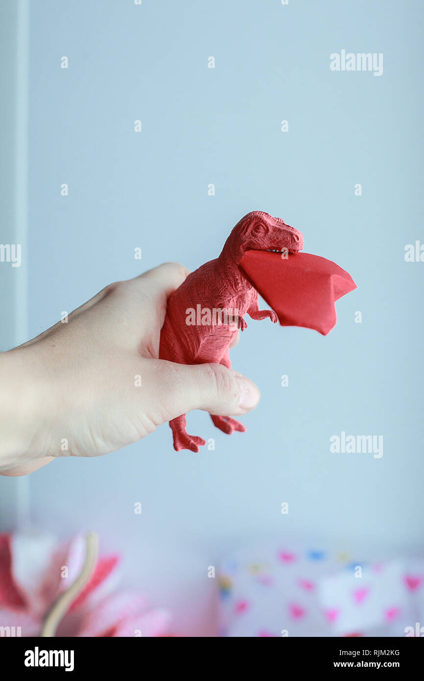 Toy dinosuar biting paper craft origami red heart, surreal trendy concept of valentines day, living coral color Stock Photo
