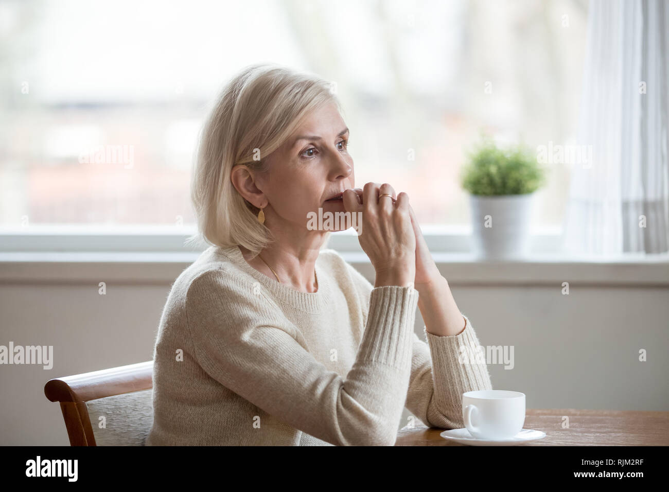 Thoughtful woman sitting at table with cup of tea  Stock Photo
