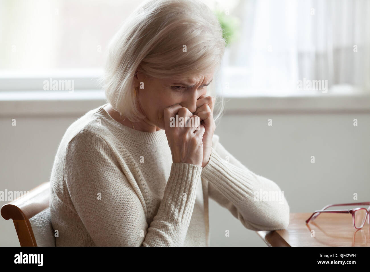 Middle aged woman sitting at table crying Stock Photo