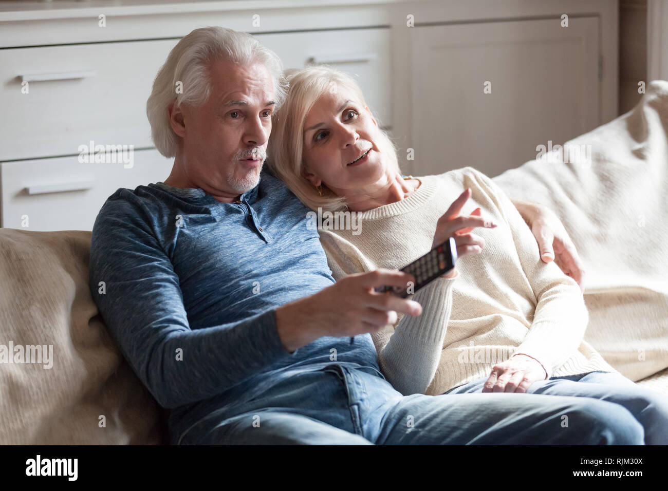 Surprised souses sitting on couch watching tv Stock Photo