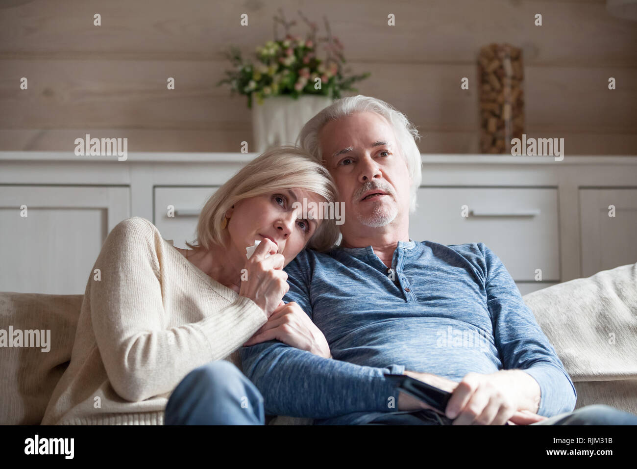 Old age spouses sitting on couch watching thriller movie Stock Photo