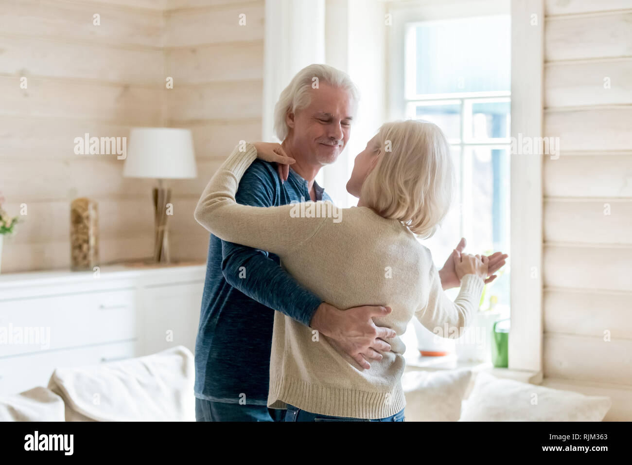 Happy aged spouses standing in living room and dancing tango Stock Photo