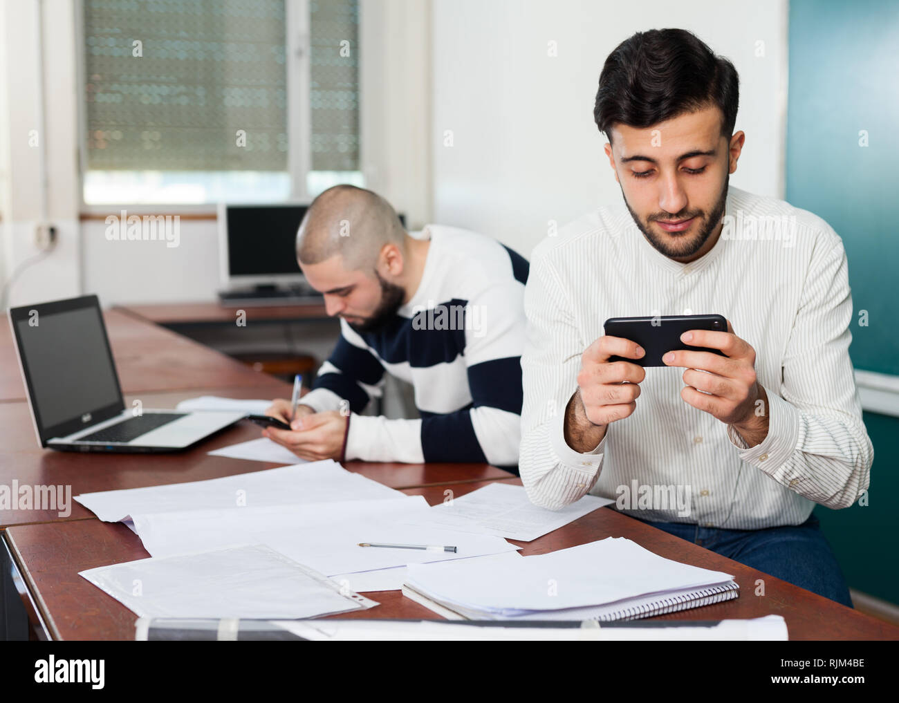 Young student distracting from his studies and watching at smartphone ...
