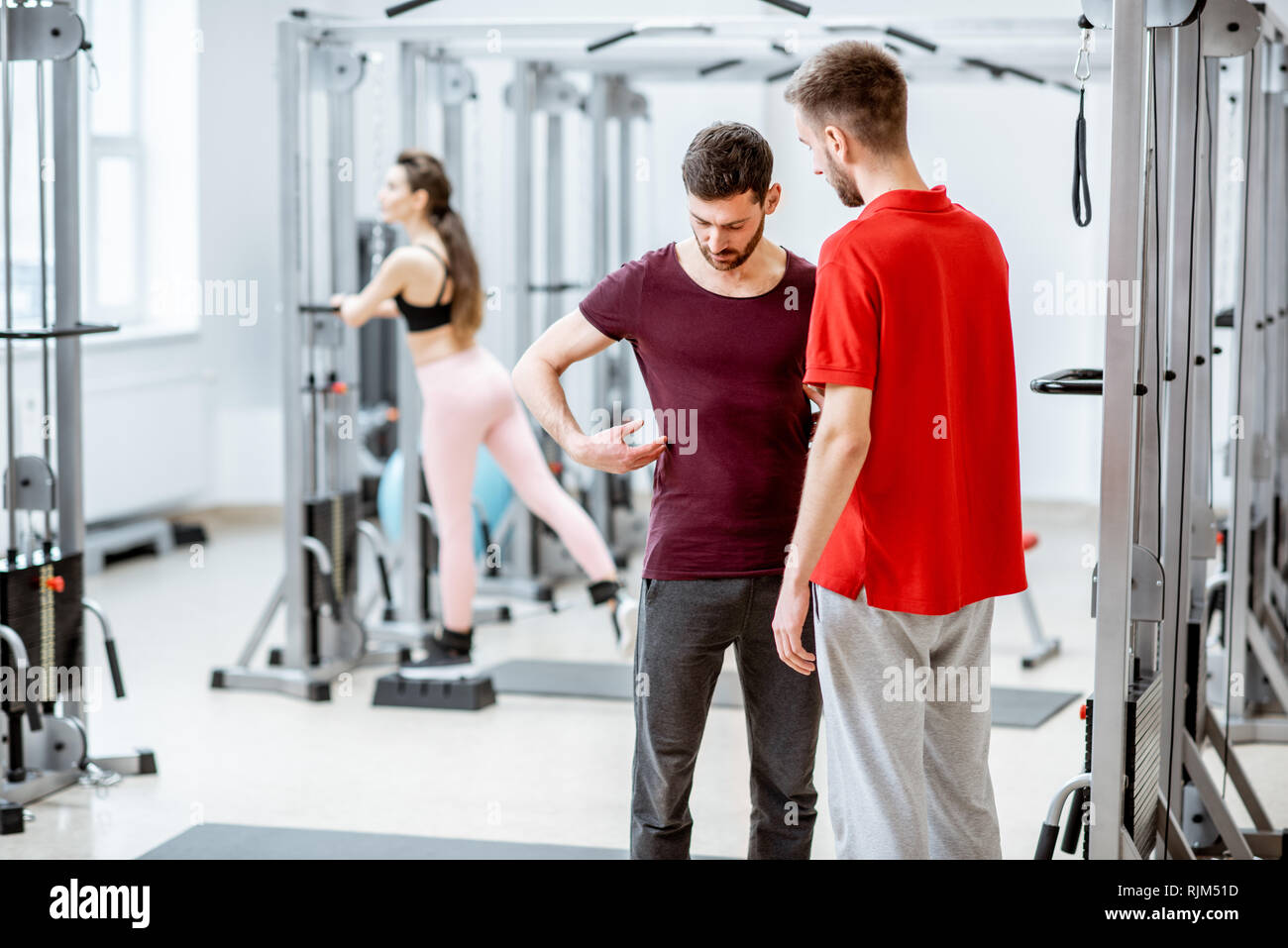 Therapist talking with man patient having problems with his back standing at the rehabilitation gym Stock Photo