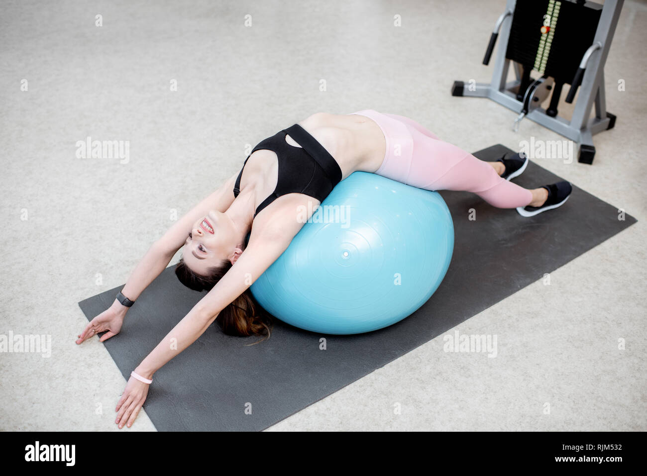 Young woman stretching on a fitness ball during the spine treatment at the rehabilitation gym Stock Photo