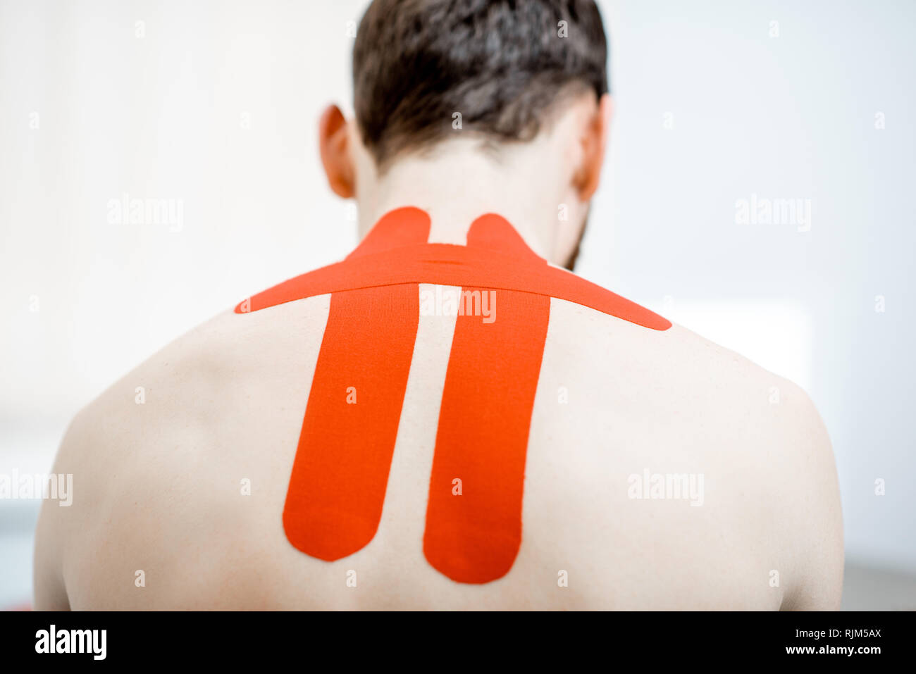 Man's neck with red kinesio tapes in the therapist office Stock Photo