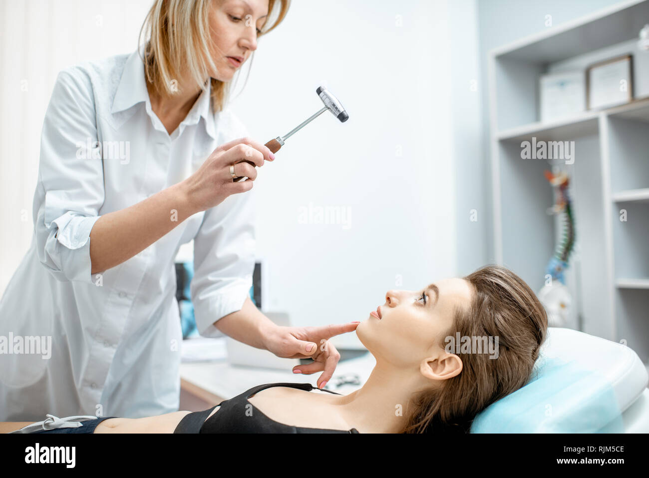 Young woman during the medical examination with neurologist testing reflexes with hammer in the office Stock Photo