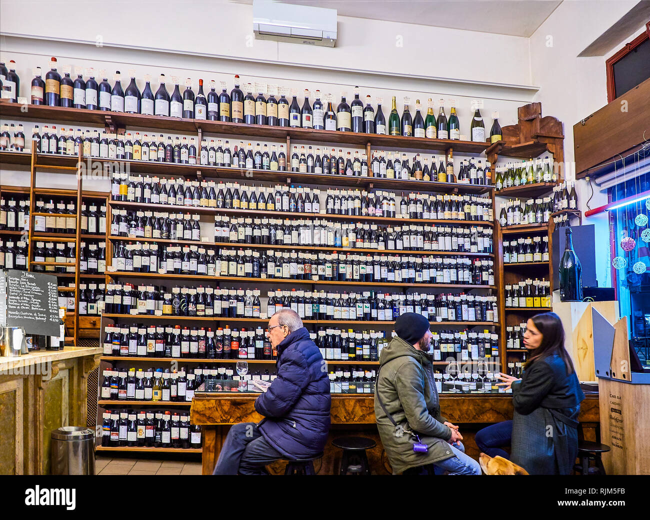 Turin, Italy - December 31, 2018. Costumers in front of a wine bottles wall of an Italian Wine Bar. Turin, Piedmont, Italy. Stock Photo
