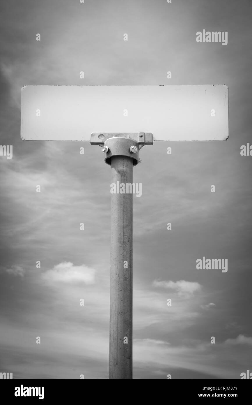 A mysterious no name metal sign on a post, similar to a street name sign, rises up to meet a dramatic sky,  seemingly with an unknown message Stock Photo