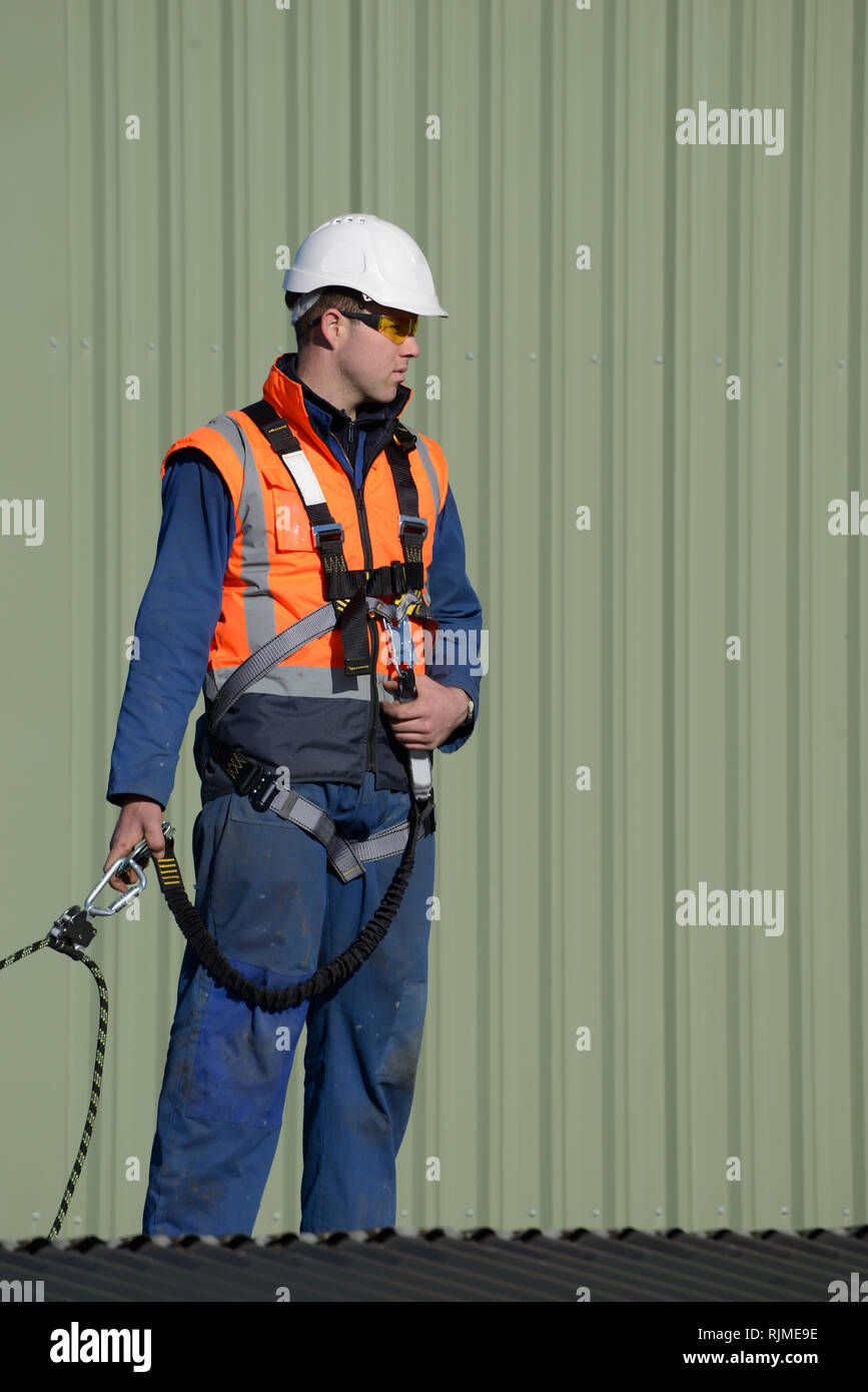 A builder wearing a safety harness while working at heights waits for instructions from the foreman Stock Photo