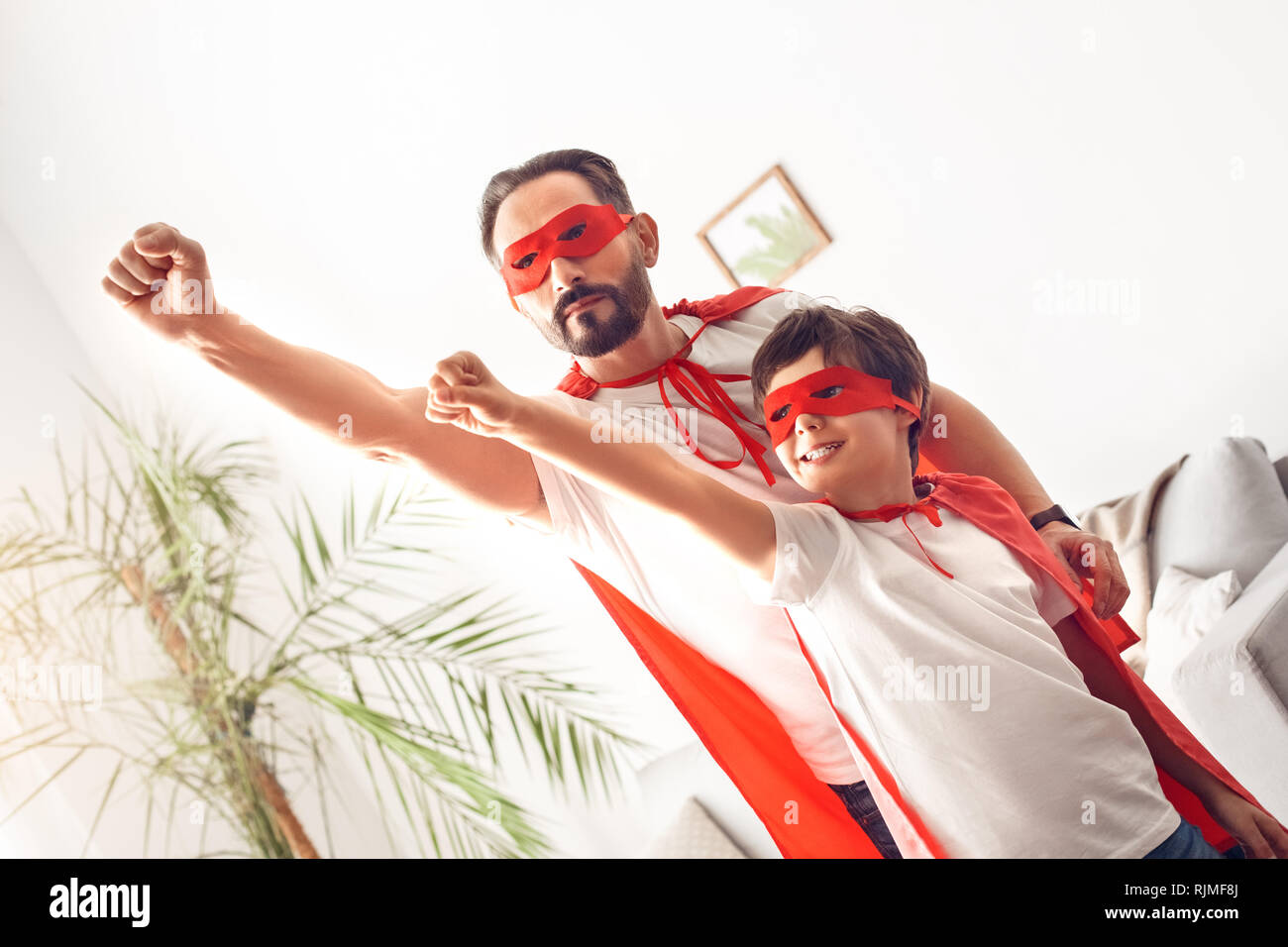 Father and son in superheroe costumes at home standing hands up flying excited Stock Photo