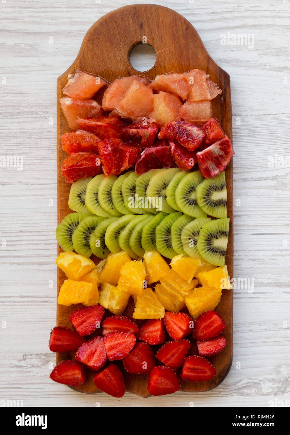Chopped fresh fruits arranged on cutting board on white wooden surface. Flat lay, overhead. Stock Photo