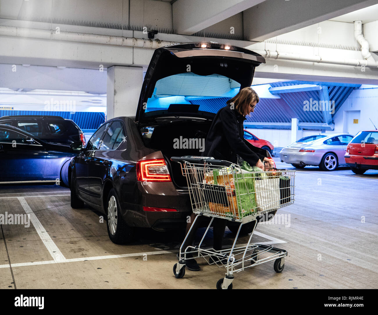 Side view of woman with shopping trolley near car putting bags with