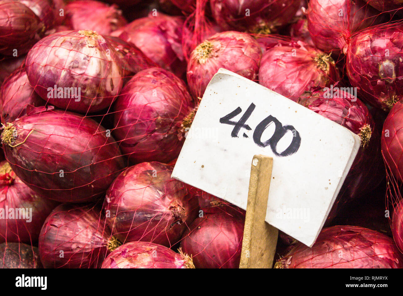 Red onions fresh and organic on sale at a vegetable stand in a food local market with the white price tag on wood stick. Stock Photo