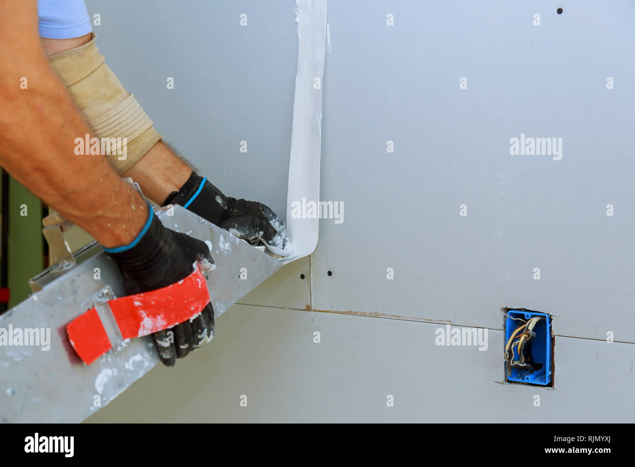 Worker Installing Gypsum Board To Wall Interior Of A Room