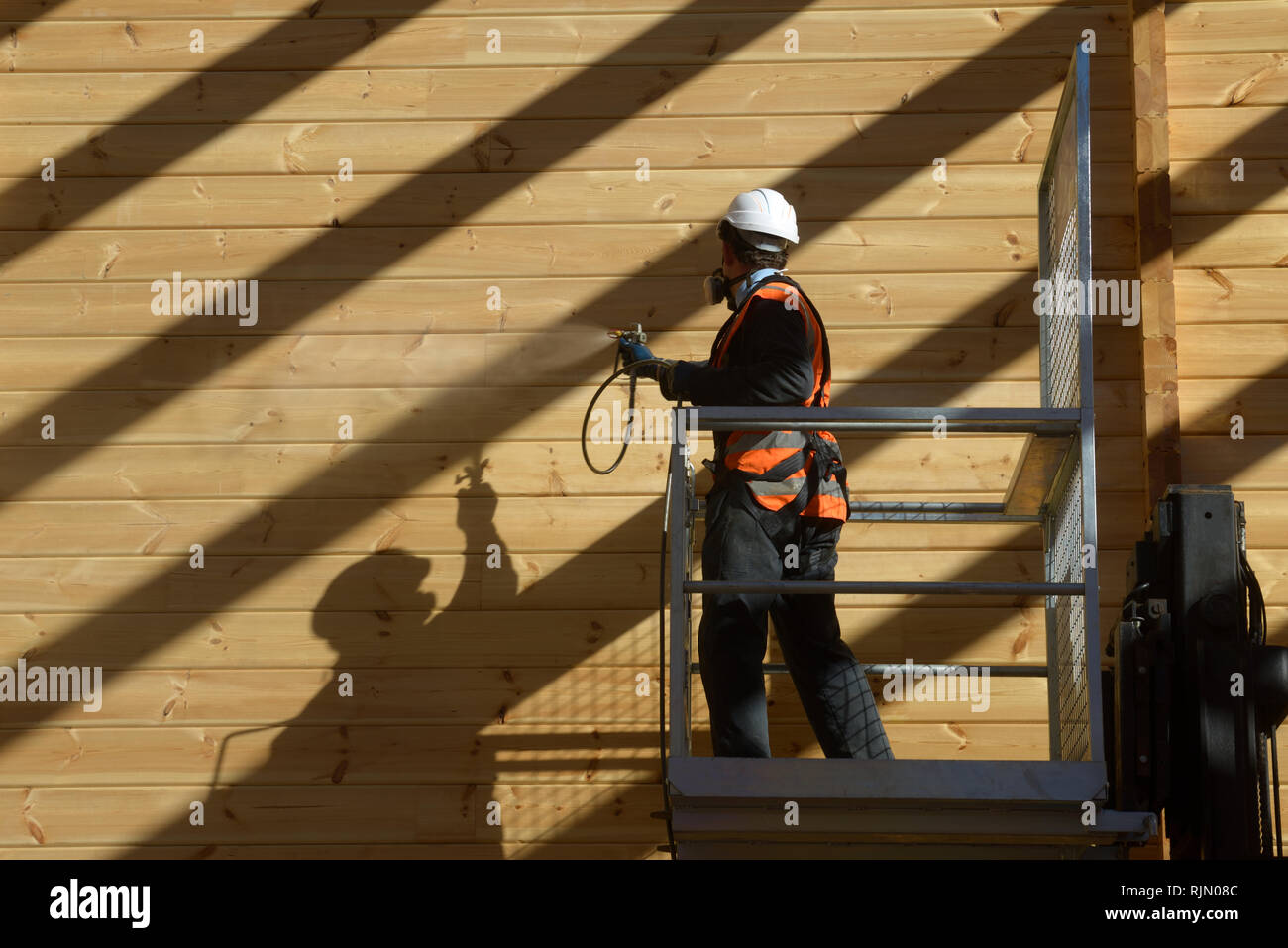 Tradesman spray painting the wall of a wooden industrial building with timber preservative Stock Photo