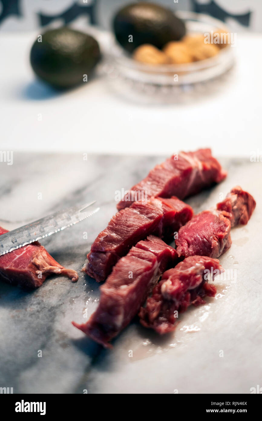 A marbled beef roast on a marble cutting board being cut up with a serrated knife. Stock Photo