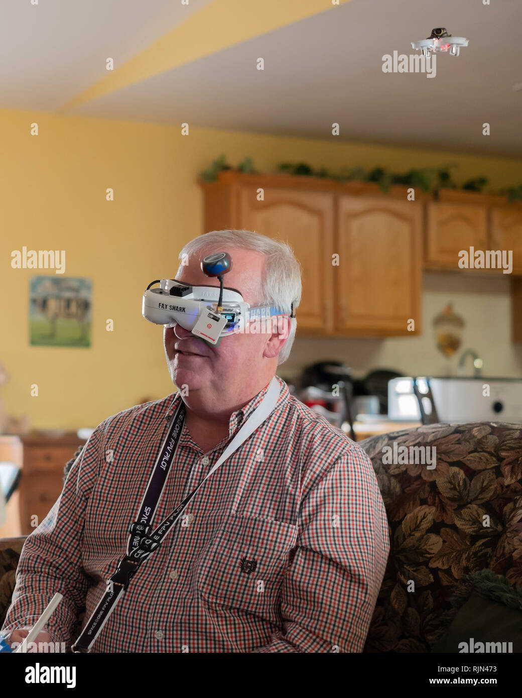 Fat Shark drone goggles worn by a 55 year old Caucasian man to visualize his small EACHINE E10 mini UFO quadcopter drone flying inside a home. USA. Stock Photo