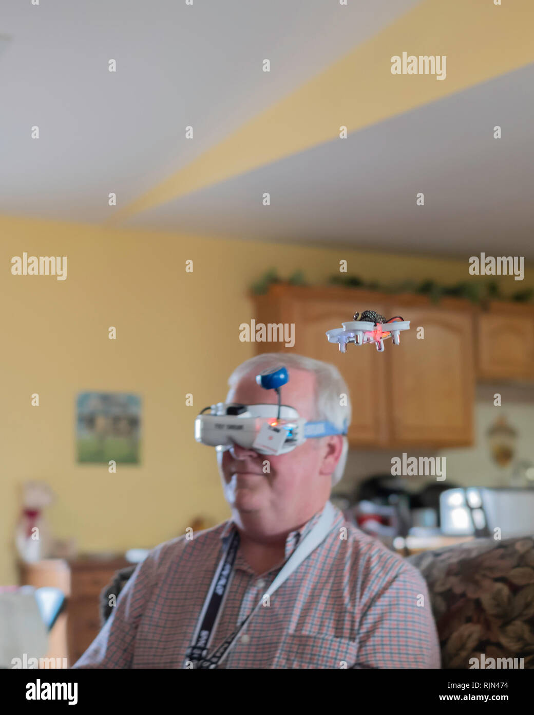 Fat Shark drone goggles worn by a 55 year old Caucasian man to visualize his small EACHINE E10 mini UFO quadcopter drone flying inside a home. USA. Stock Photo