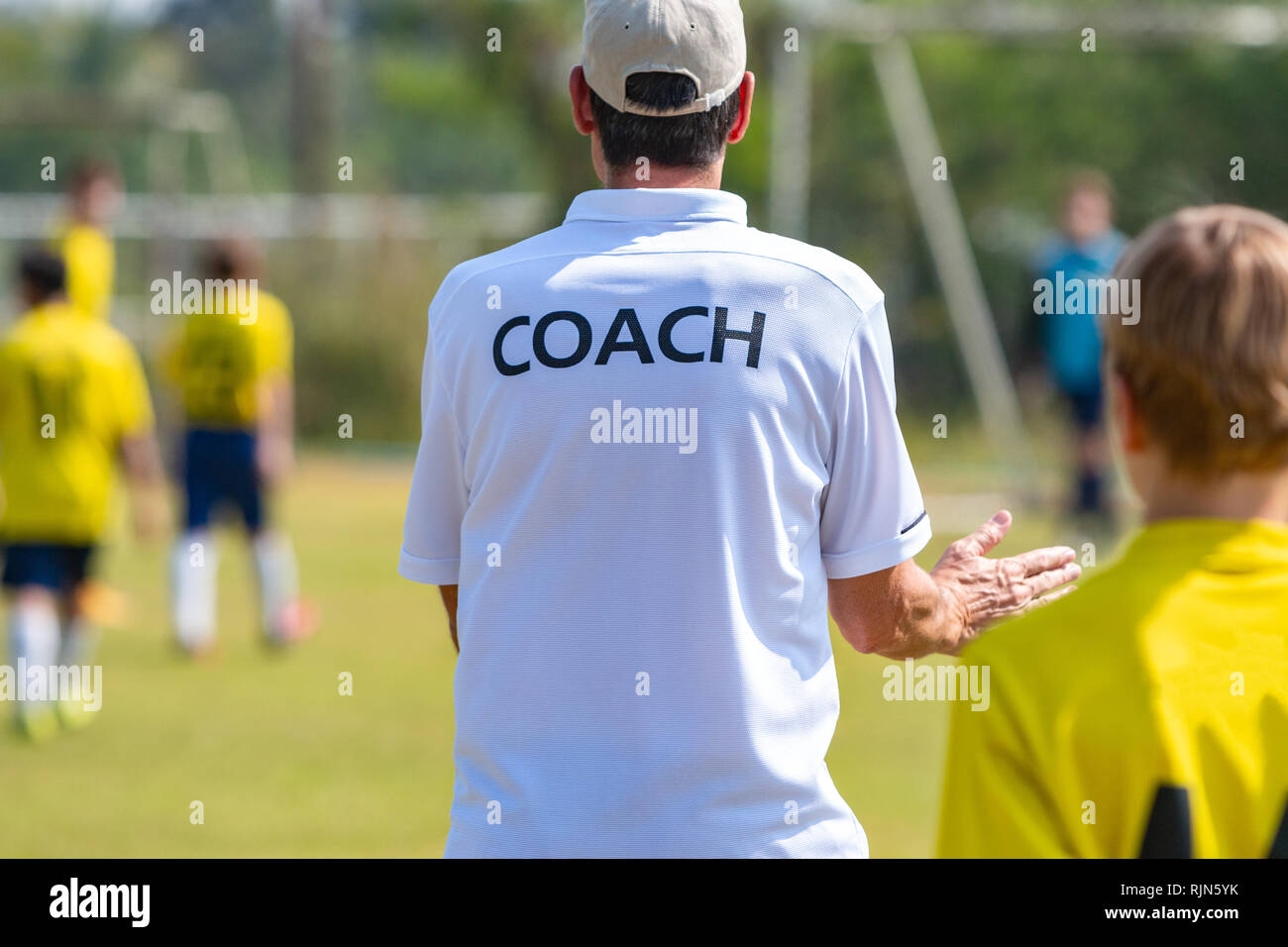 Back of football coach wearing white COACH shirt at an outdoor sport
