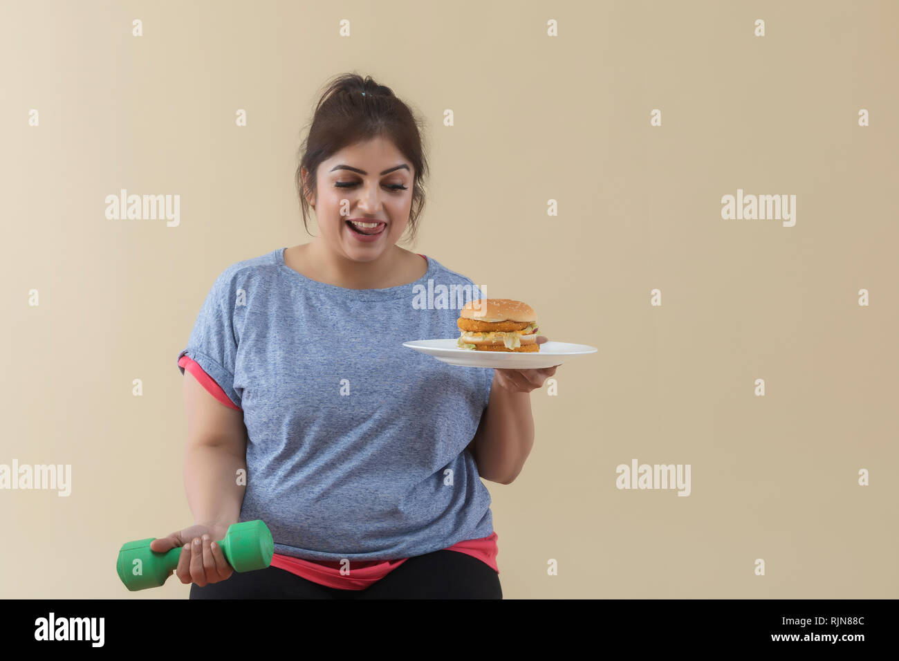 Smiling Overweight Woman holding a burger and dumbbell Stock Photo