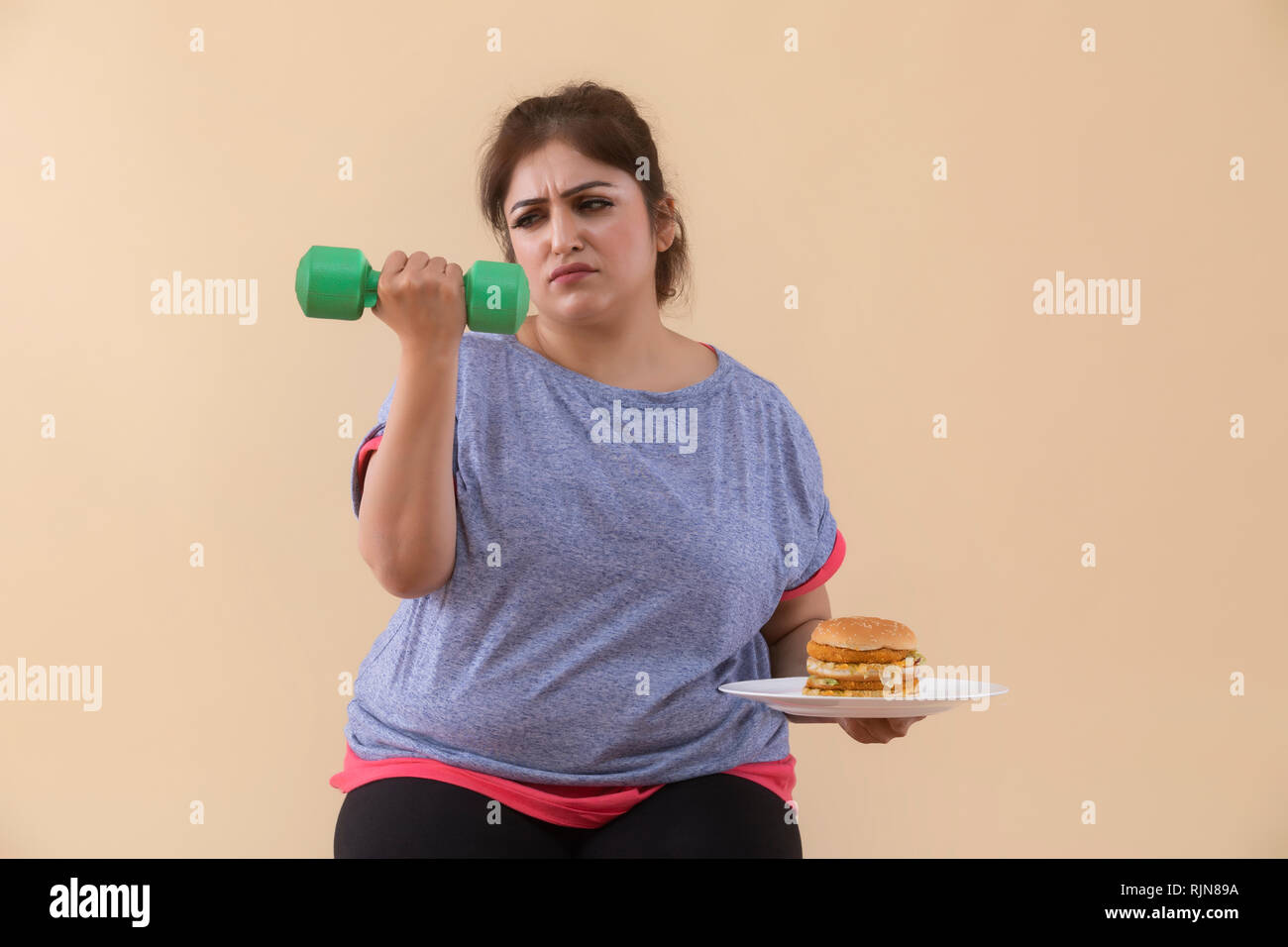 Sad Overweight Woman holding a burger and dumbbell Stock Photo