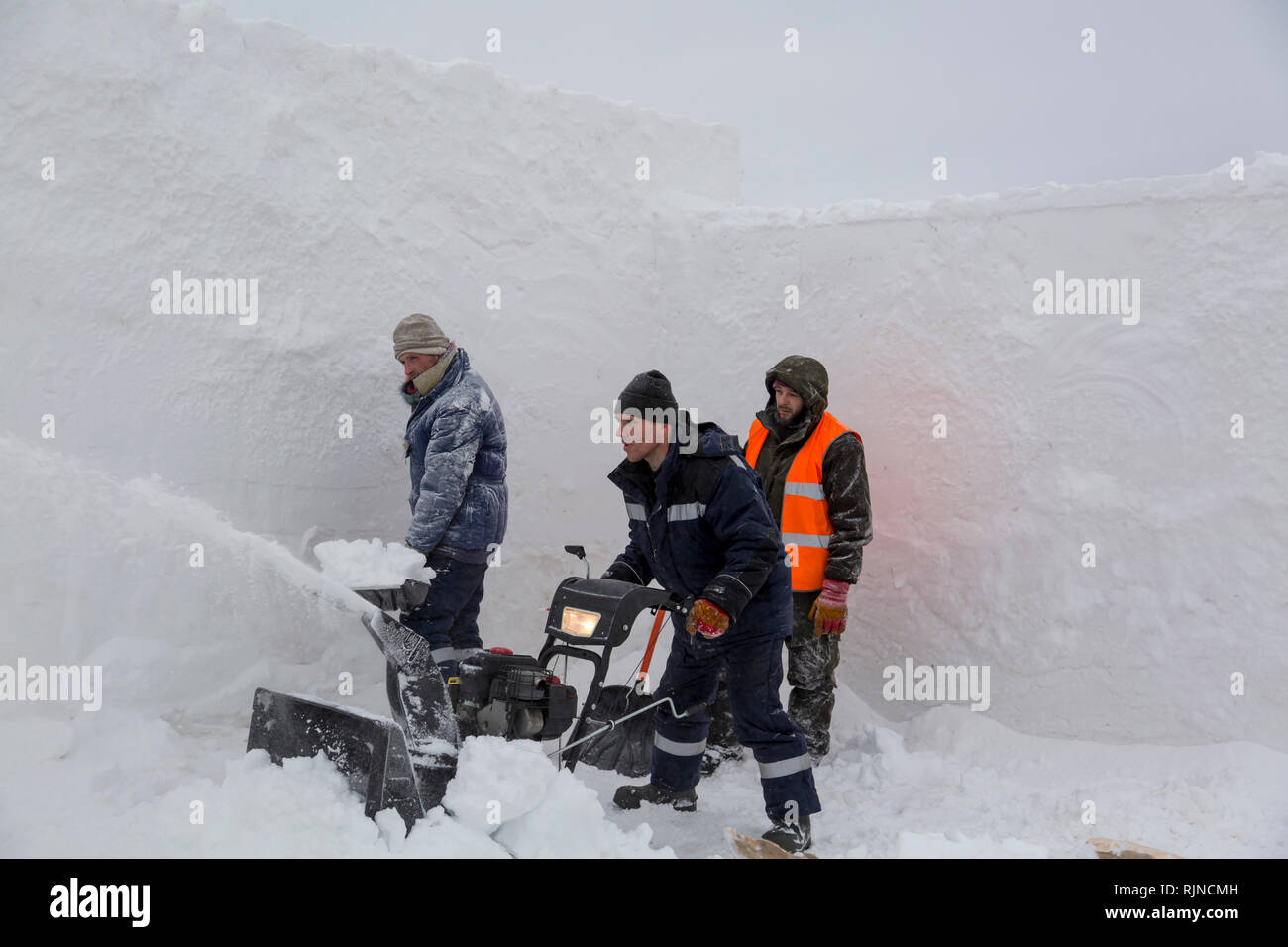 Workers remove snow in a blizzard using a snowplow Stock Photo - Alamy