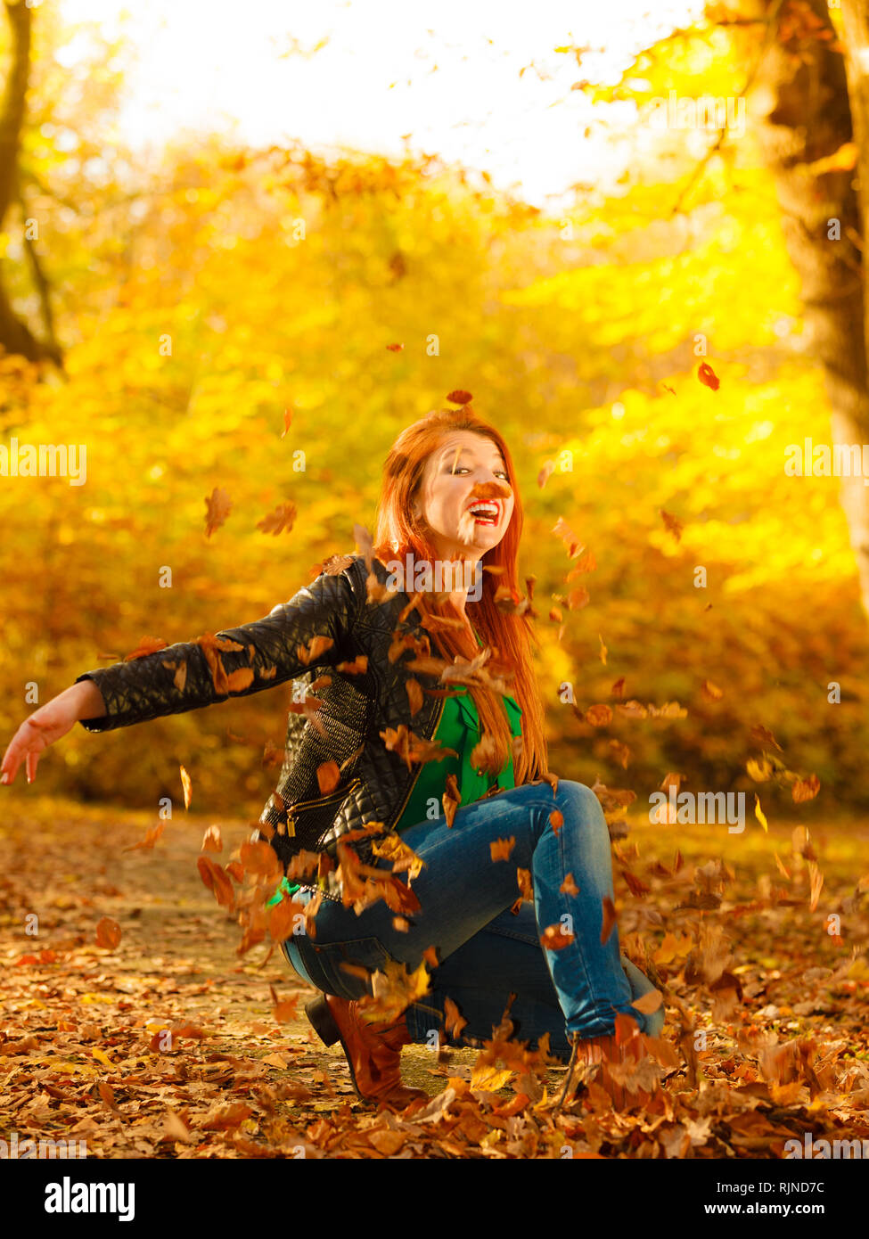 Happiness carefree leisure concept. Redhaired long hair woman relaxing in autumn park throwing leaves up in the air. Beautiful girl in orange forest f Stock Photo