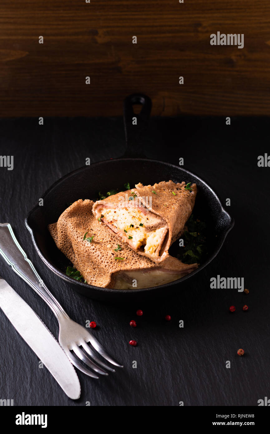 Food concept homemade Ham and Cheese Crepe in iron skillet cast on black slate background Stock Photo
