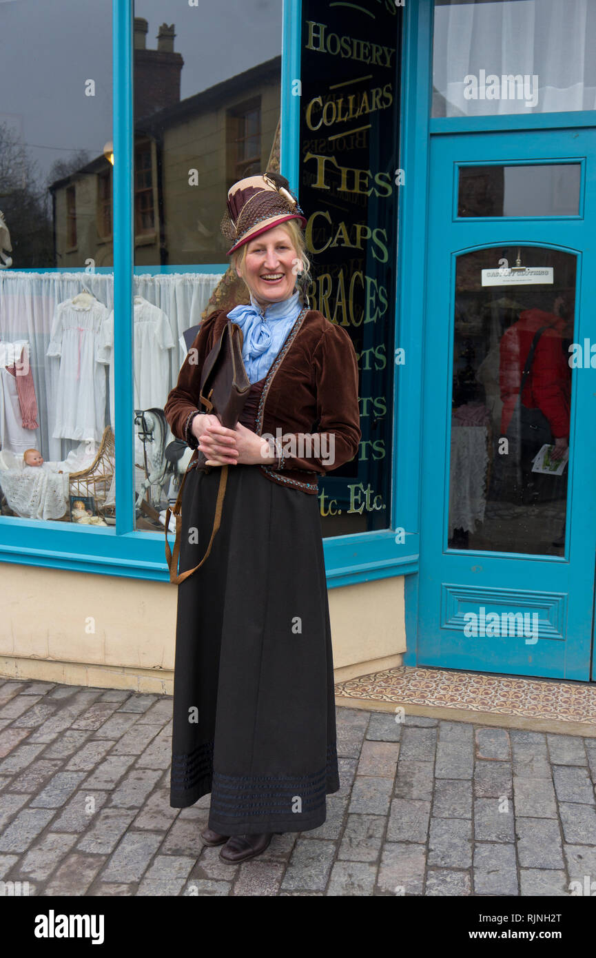 Smiling lady volunteer, in stylish Victorian costume, outside a draper's store, Blists Hill Victorian Town, Shropshire, UK Stock Photo