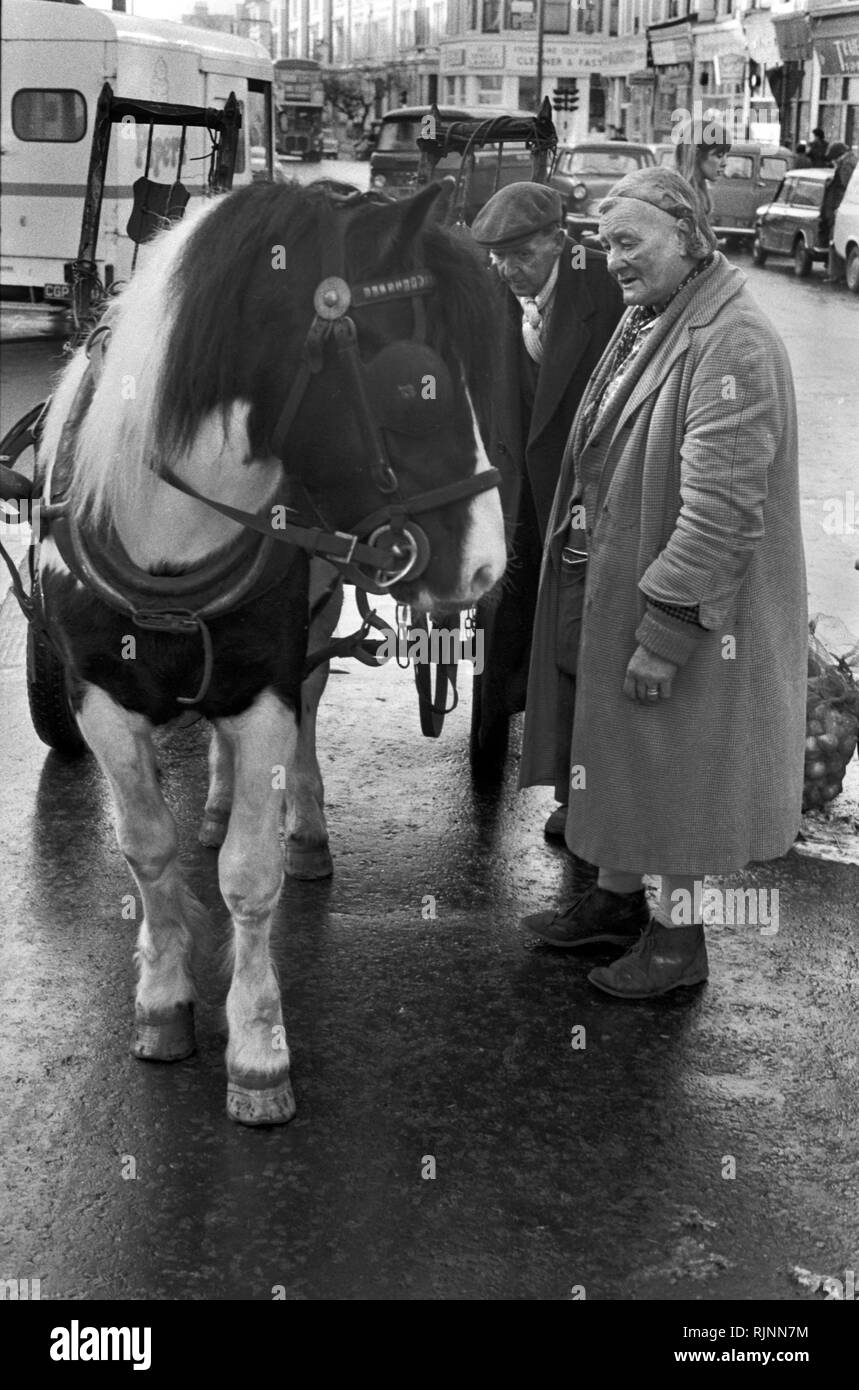 Rag and Bone man with his wife partner and  his horse and cart. She has a market street stall selling fest vegetables. Notting Hill area of West London 1970. Collecting scrap for recycling re-cycling 1970s UK. HOMER SYKES Stock Photo