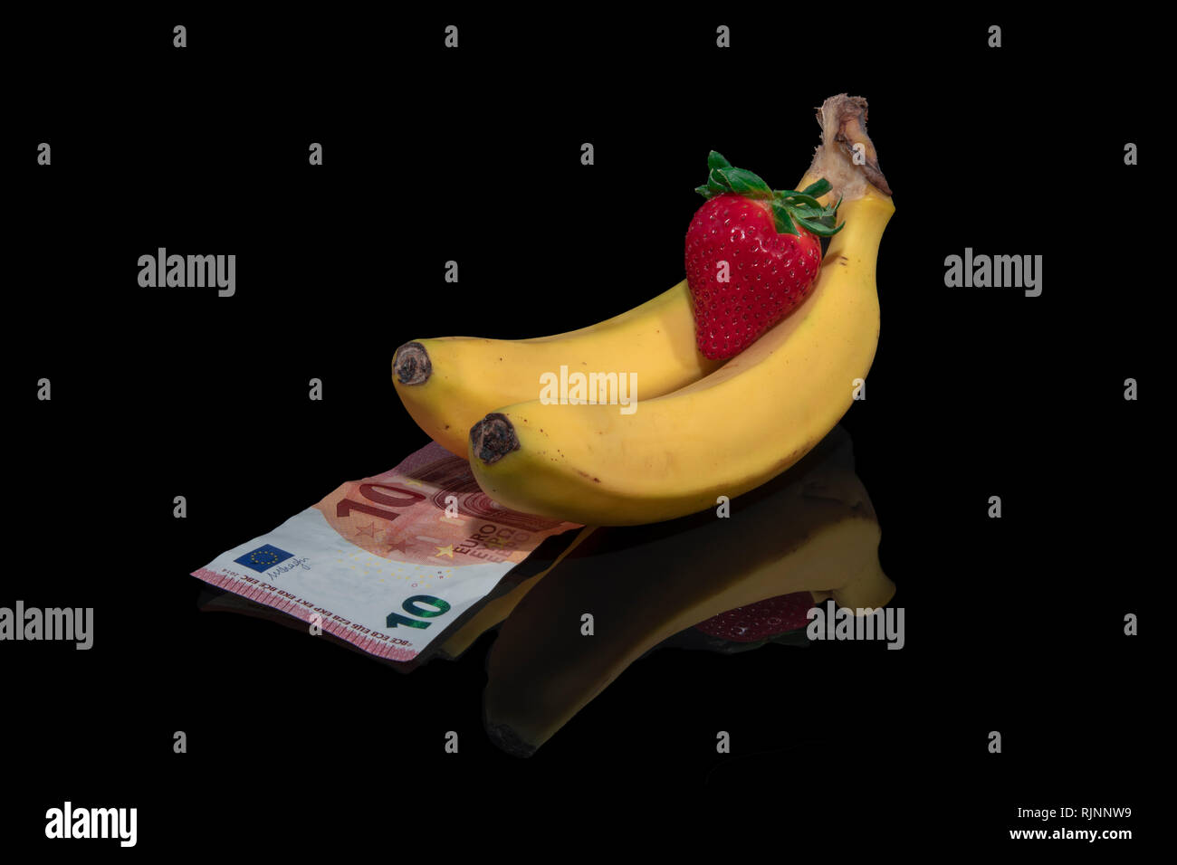 Two Bananas,strawberry and money with reflection on a black background Stock Photo